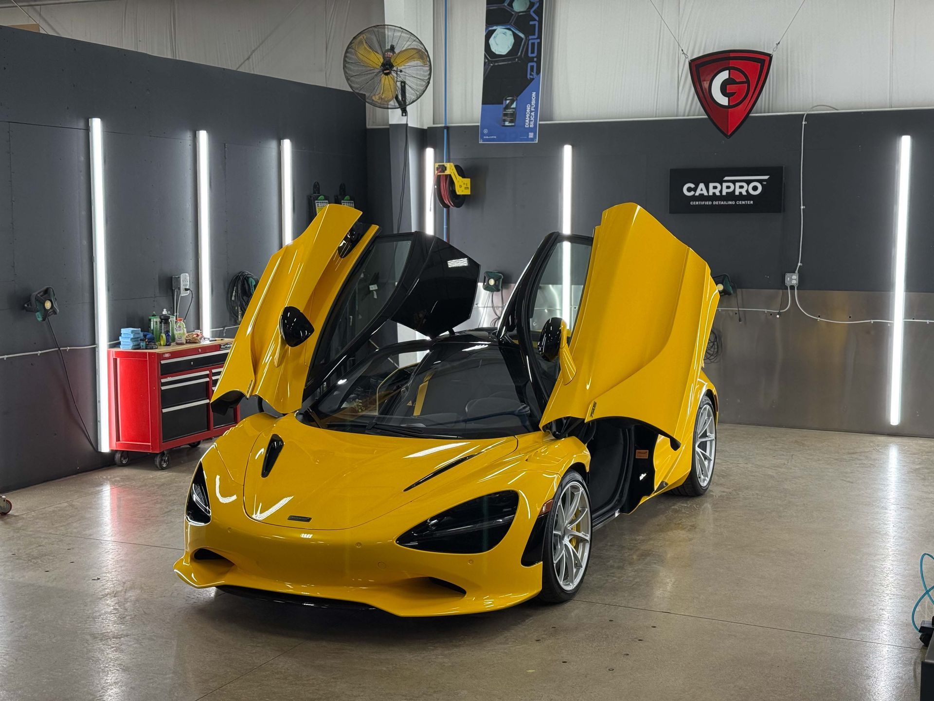 Yellow McLaren sports car with doors open in a detailing garage, under bright lights.
