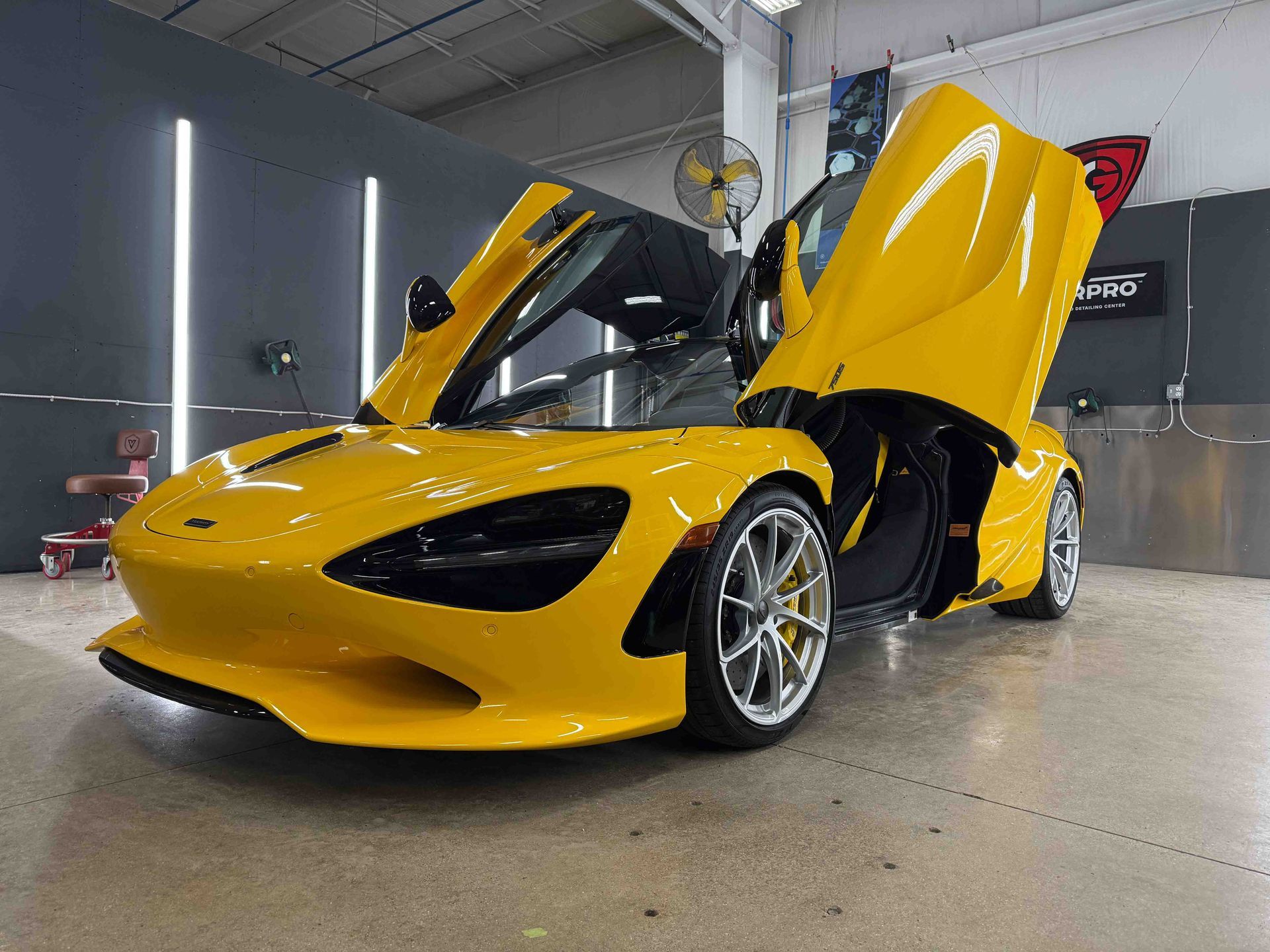 Yellow McLaren sports car with doors open, in a garage setting.