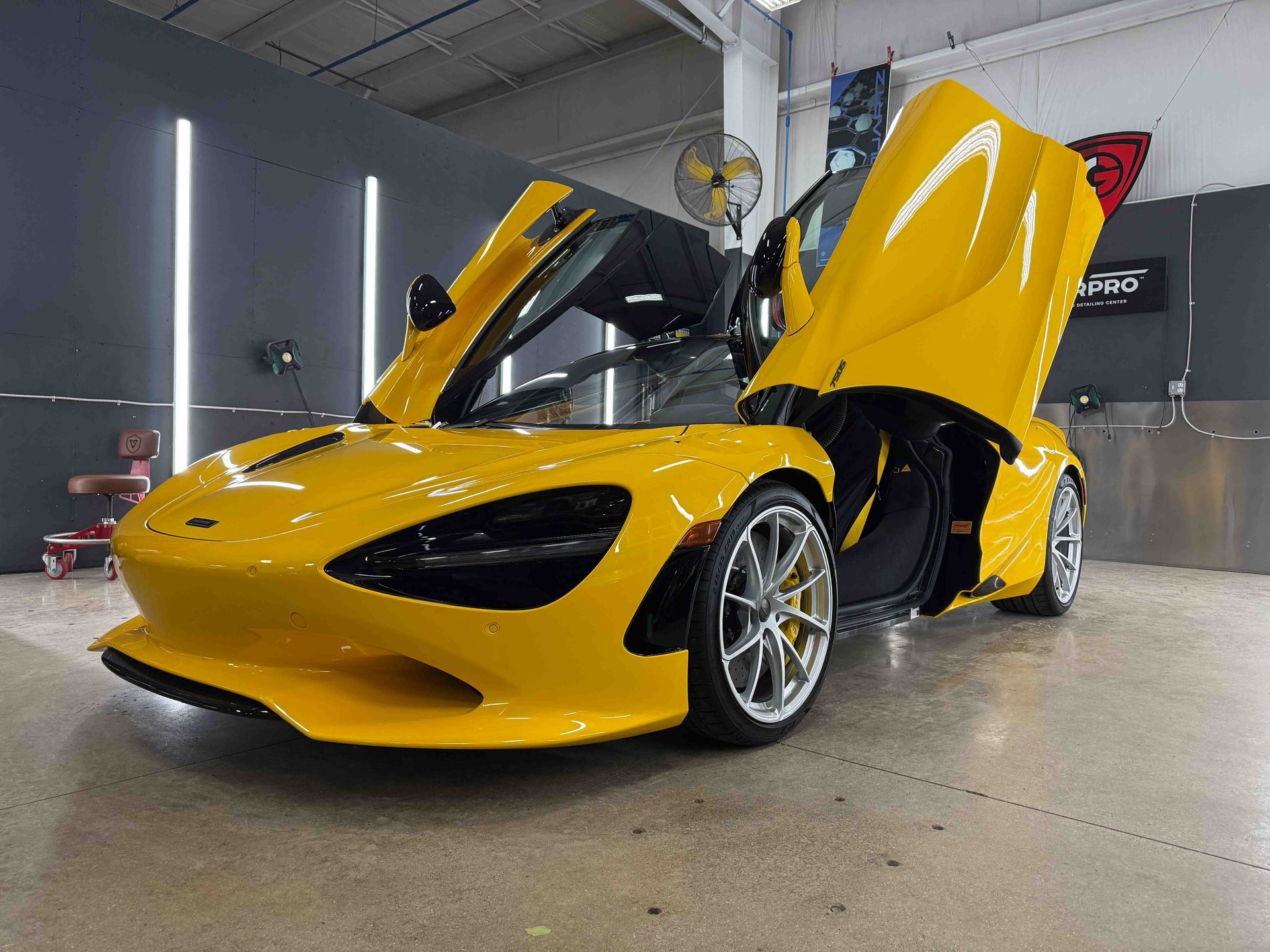 Yellow McLaren sports car with doors open, inside a garage.