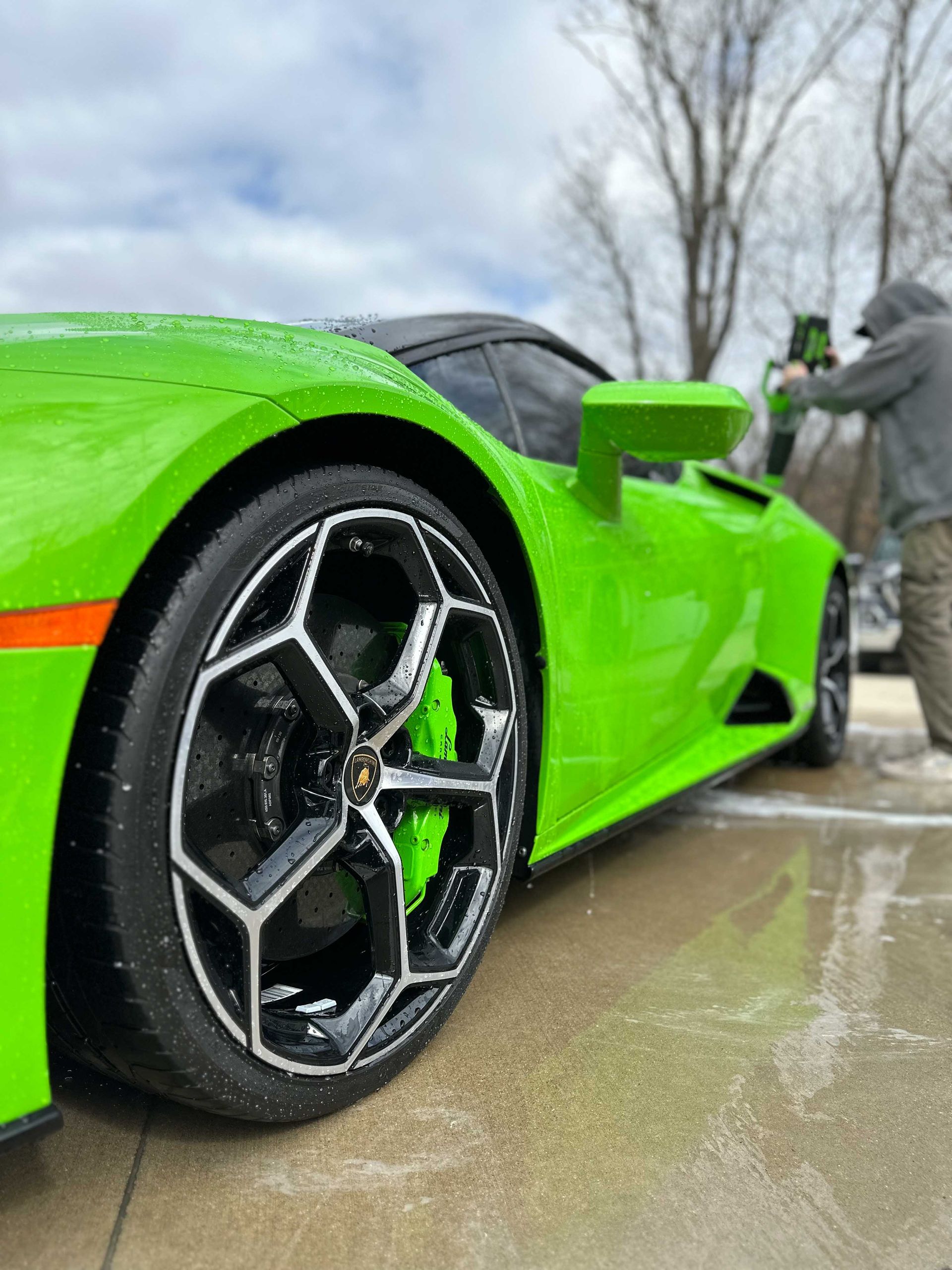 Bright green Lamborghini being washed. Person in gray hoodie sprays the car.