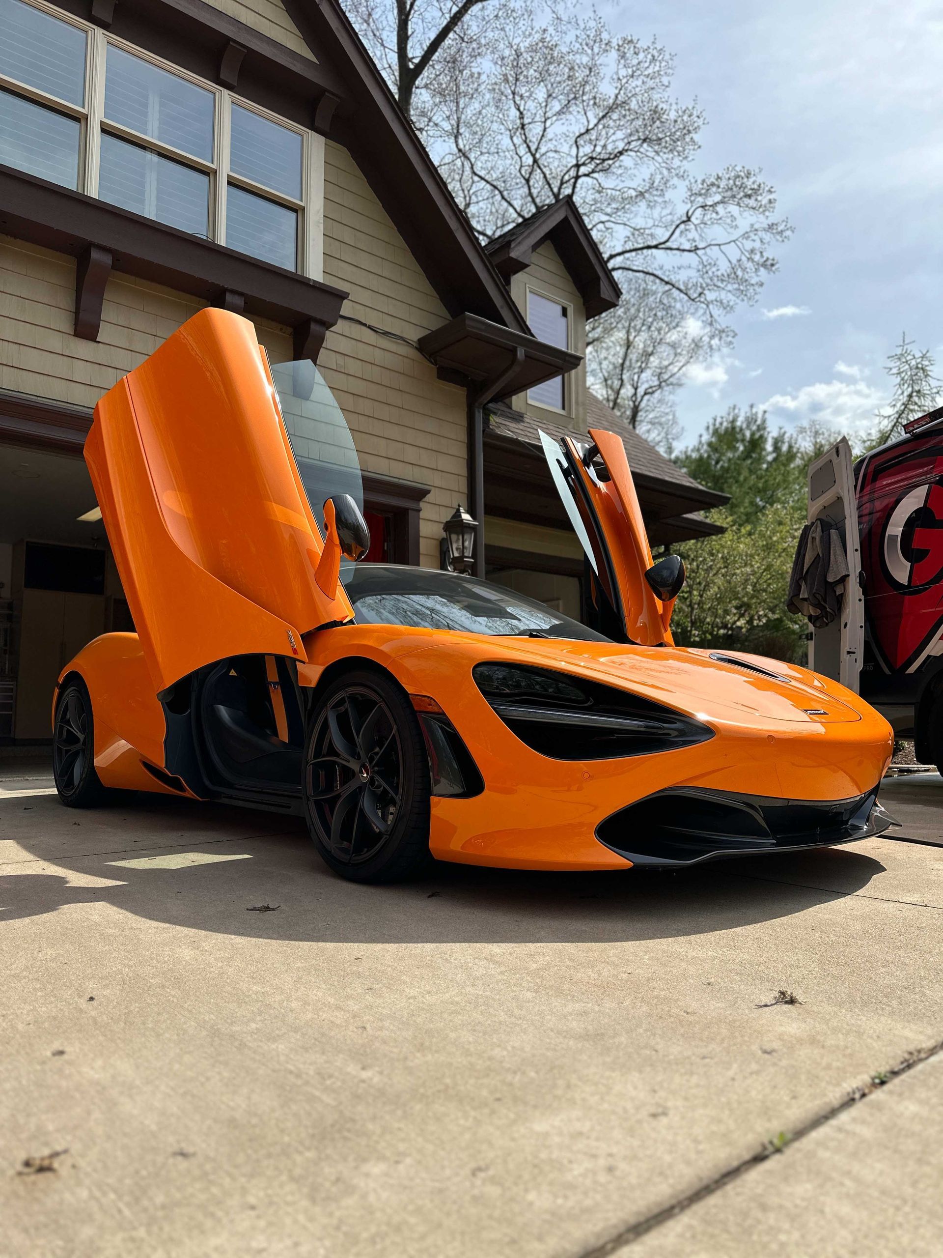Orange McLaren sports car with doors open in a driveway.