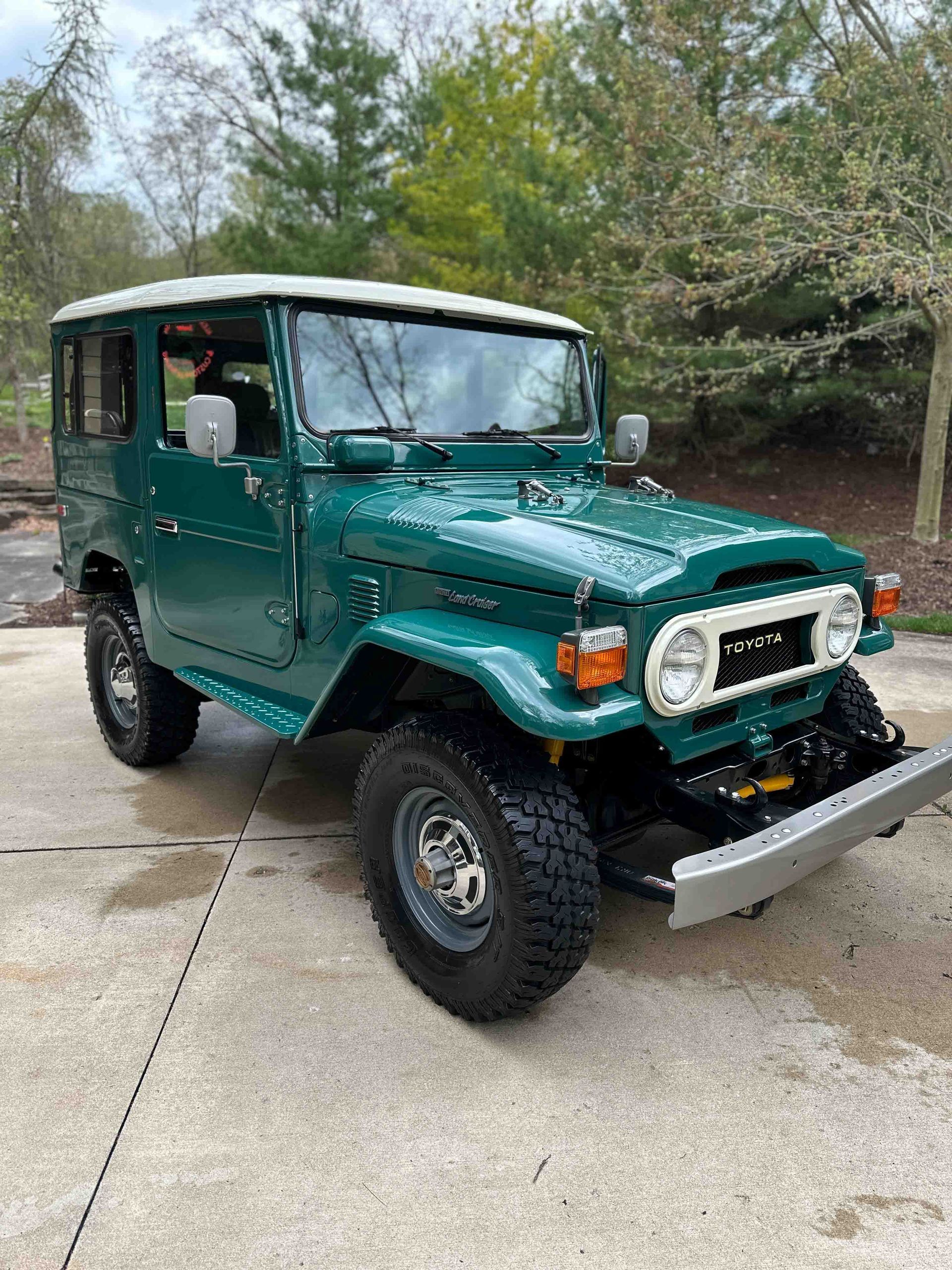 Green Toyota Land Cruiser with white roof parked on a concrete surface, tires are dark and rugged.