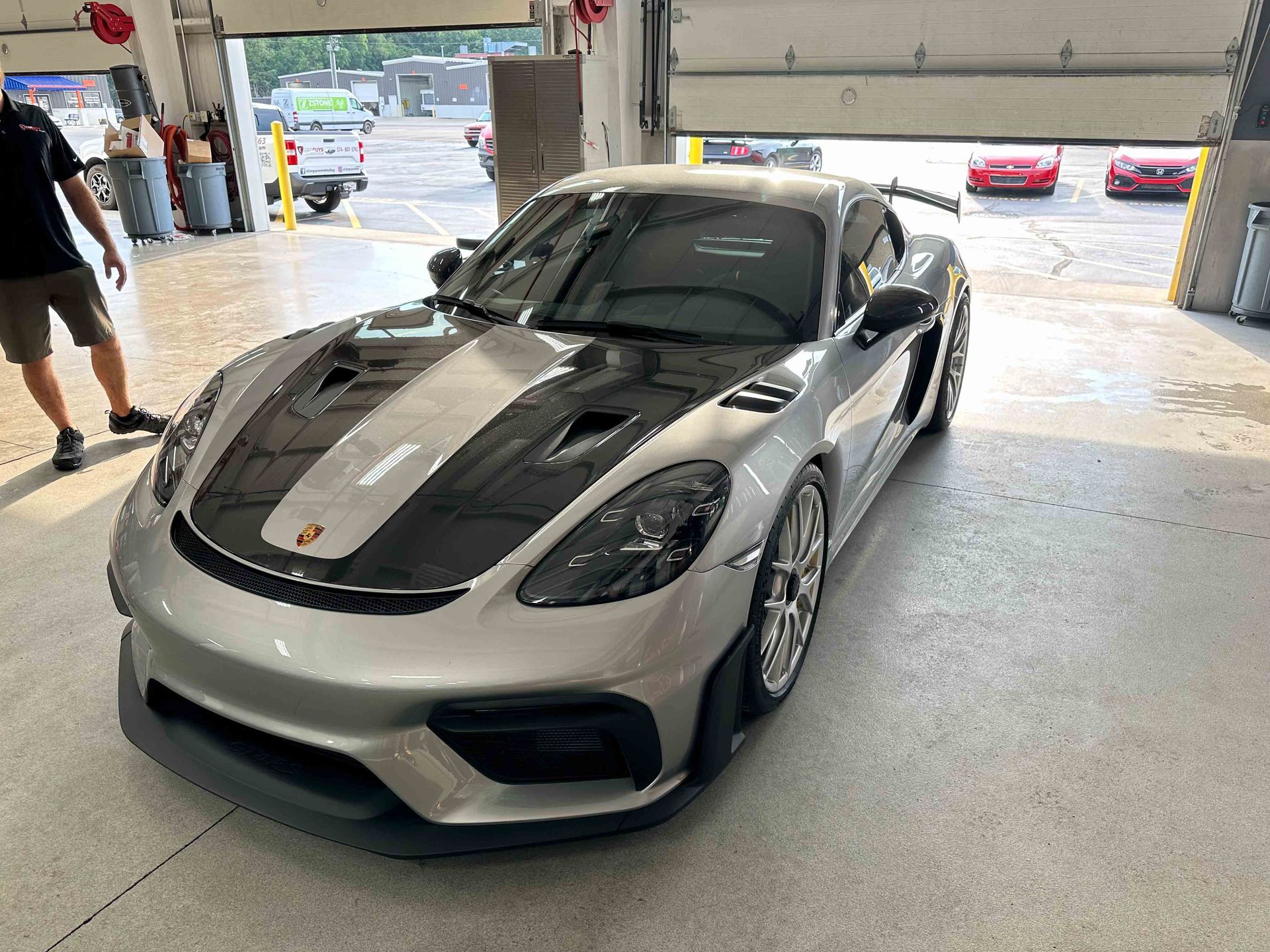Silver Porsche Cayman GT4 with black hood in a garage.
