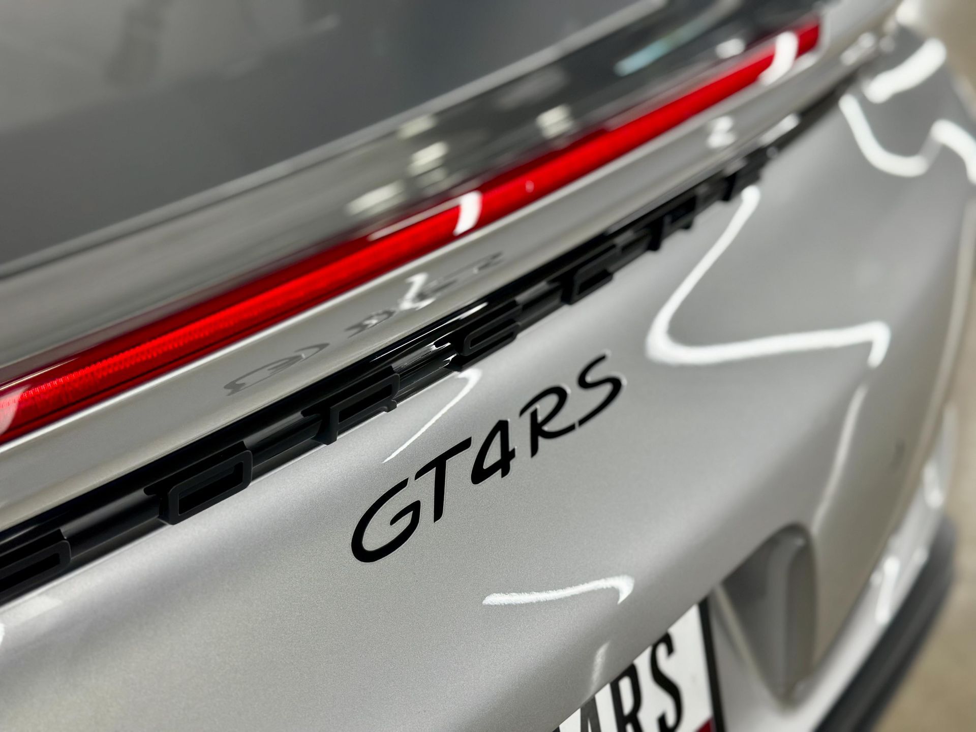 Silver Porsche GT4RS rear with black lettering, red taillight, and black vents.