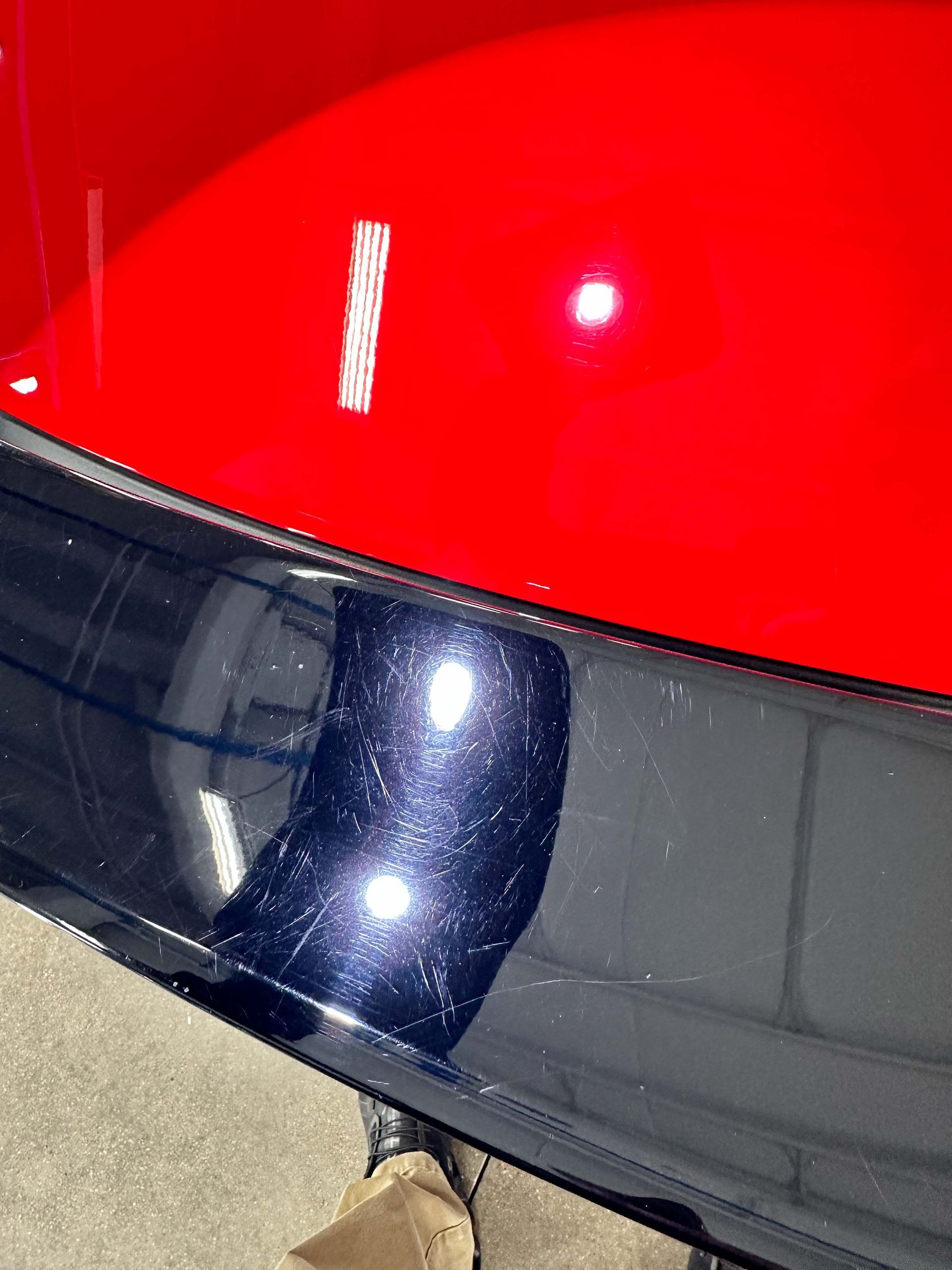 Red car paint above a blue bumper with visible scratches, indoors.
