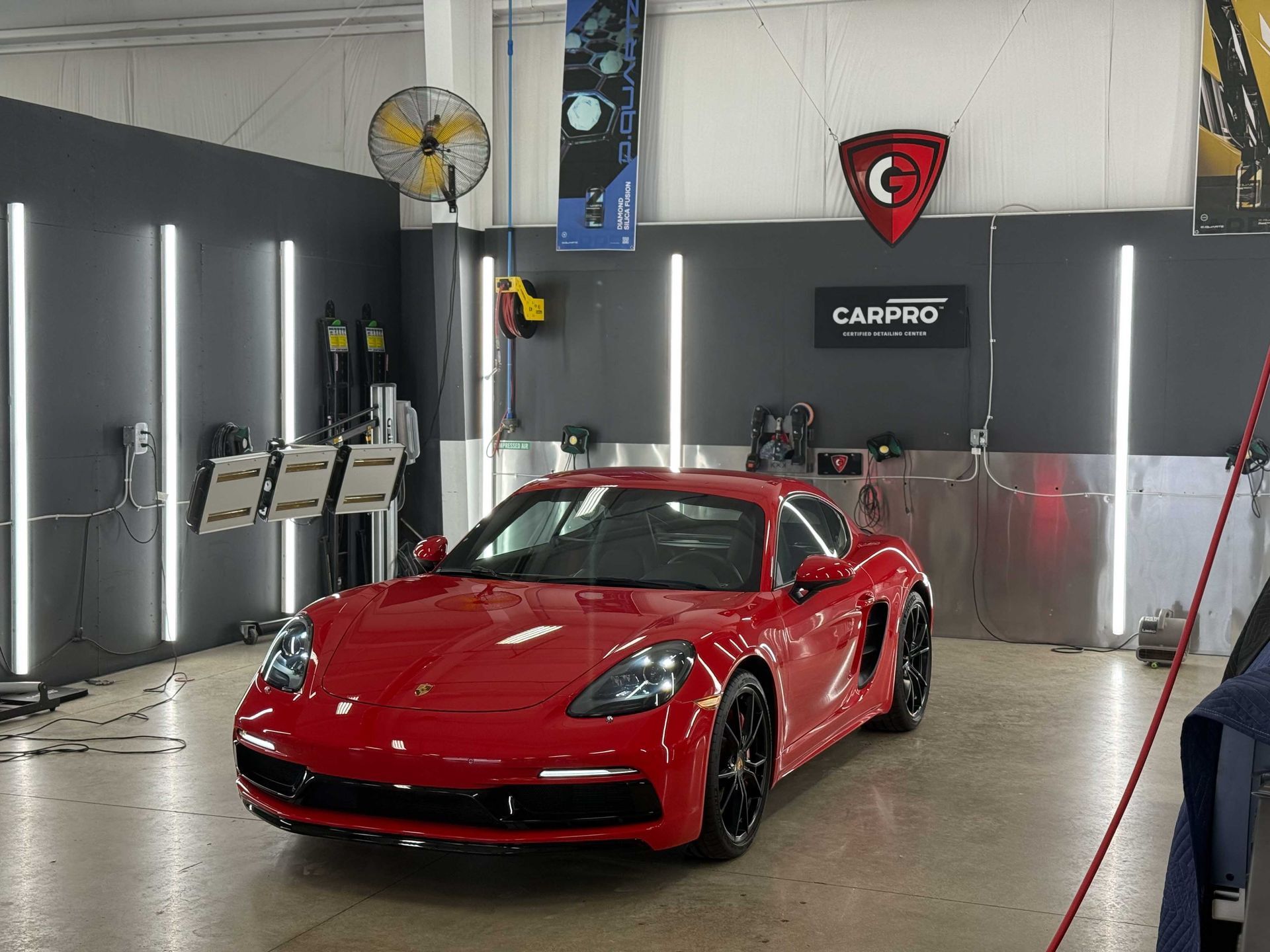 Red Porsche sports car inside a detailing shop with vertical lights and equipment.