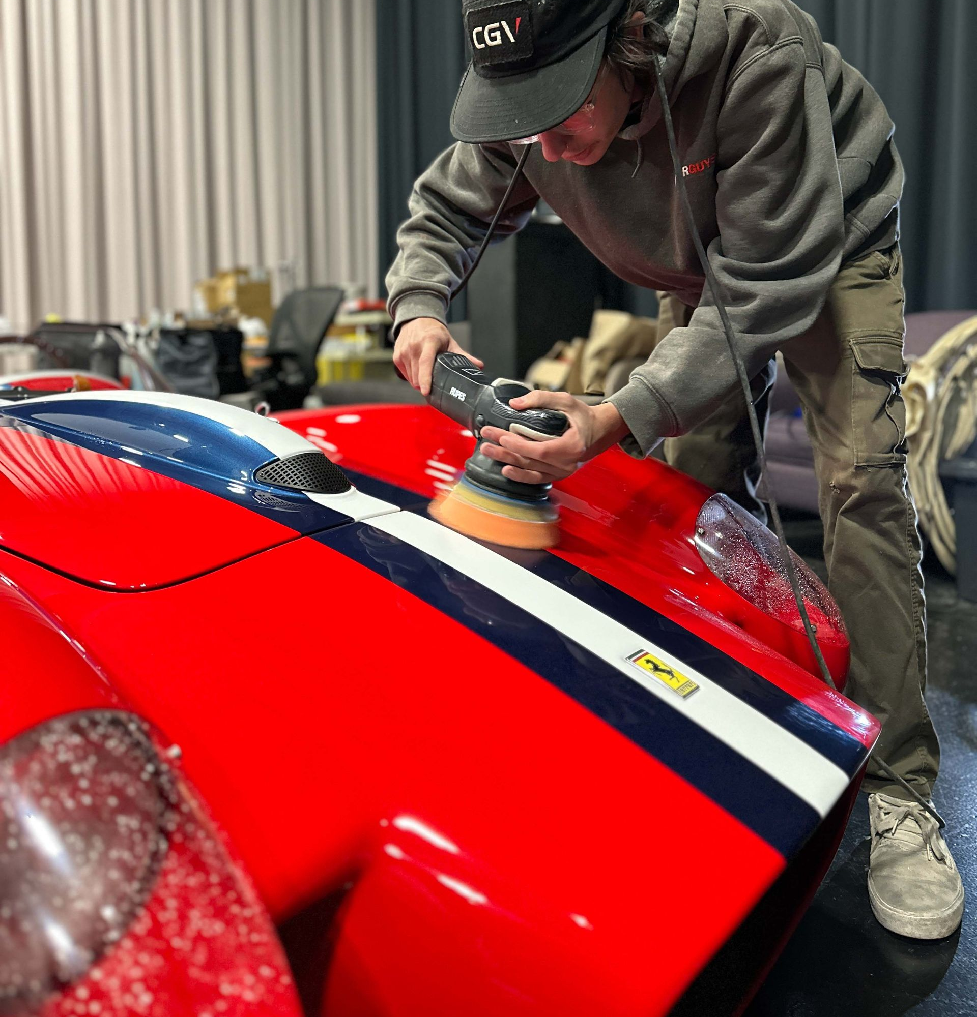 A person wearing black gloves is polishing the hood of a red car.