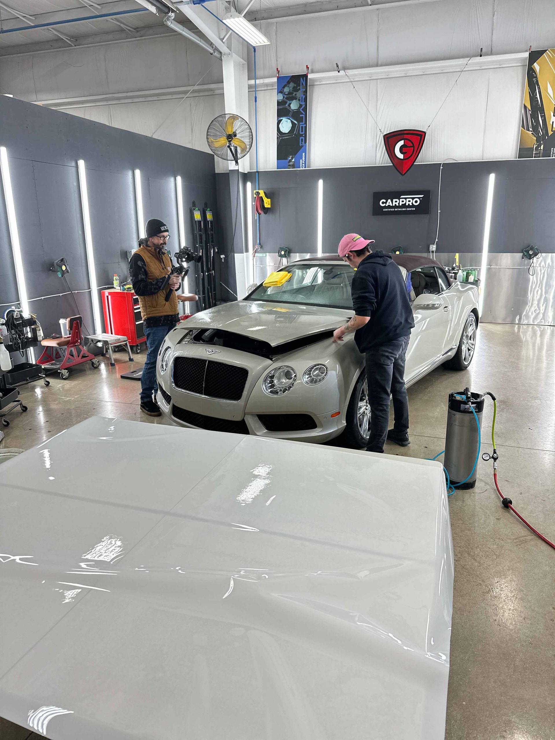 A person wearing black gloves is polishing a black car