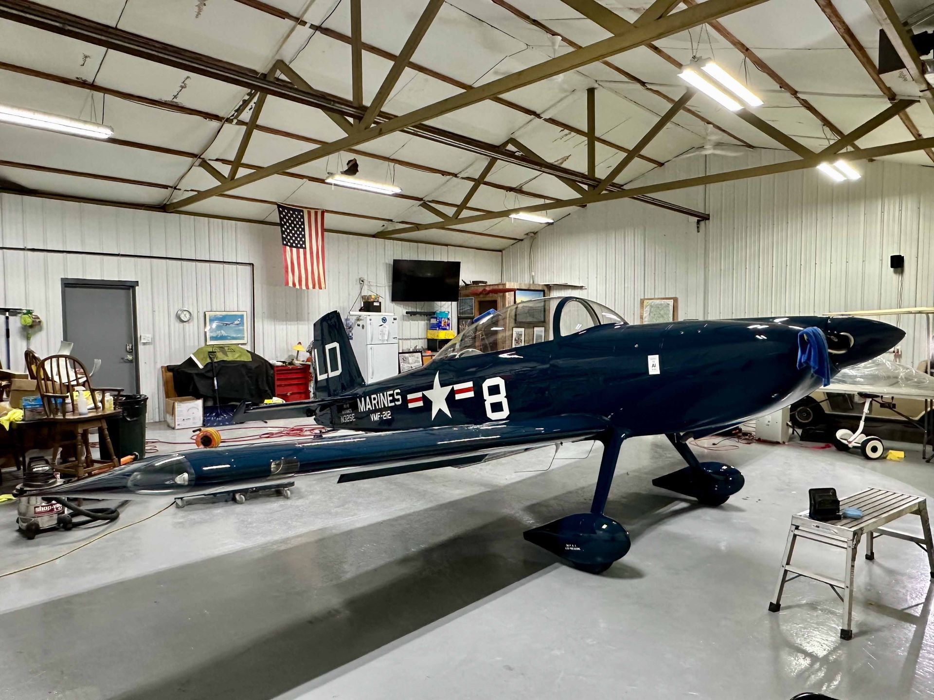 Dark blue airplane inside a hangar, with an American flag hanging on the wall.