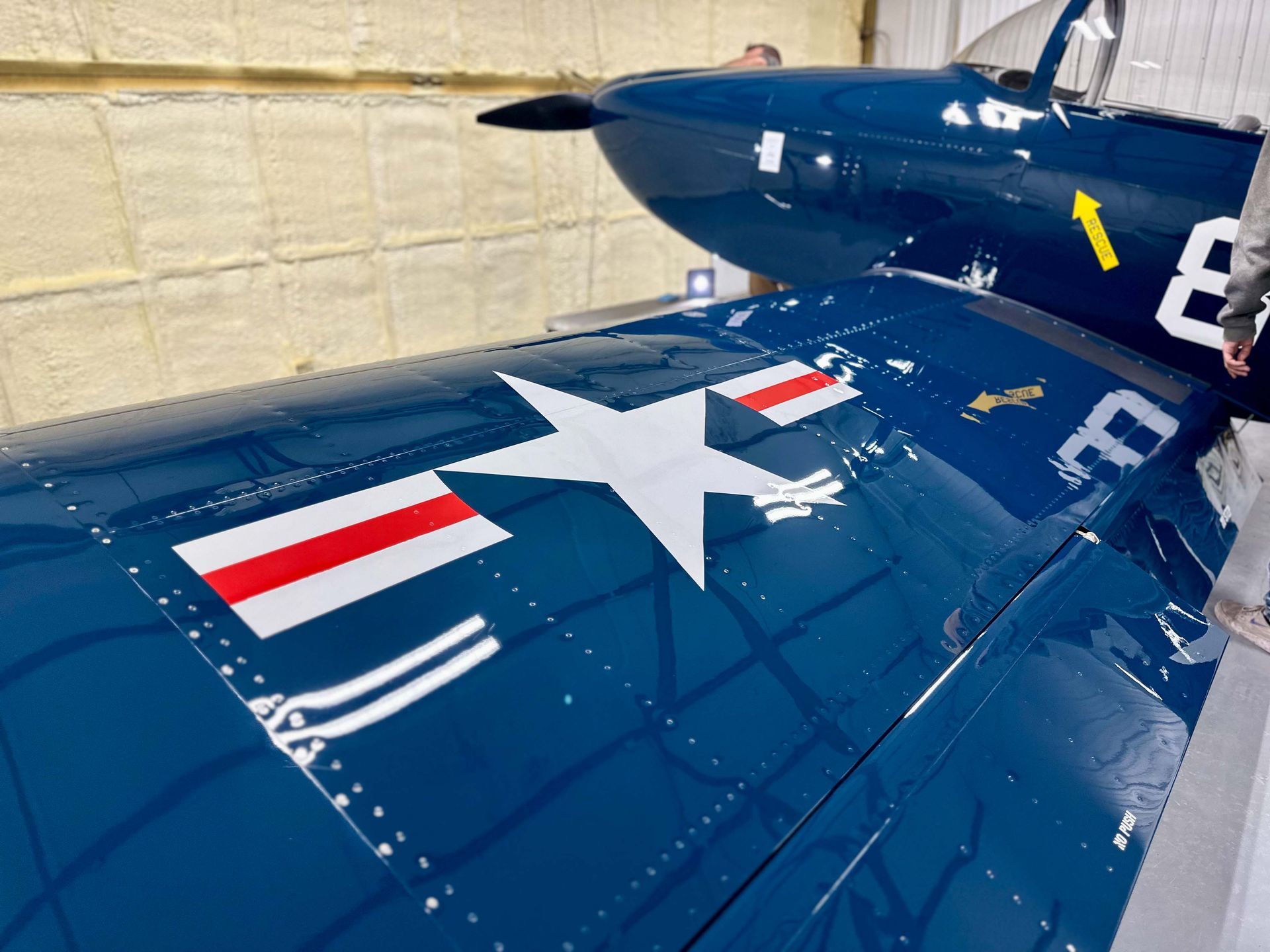 Blue airplane wing with white star insignia and red stripes, parked in hangar.