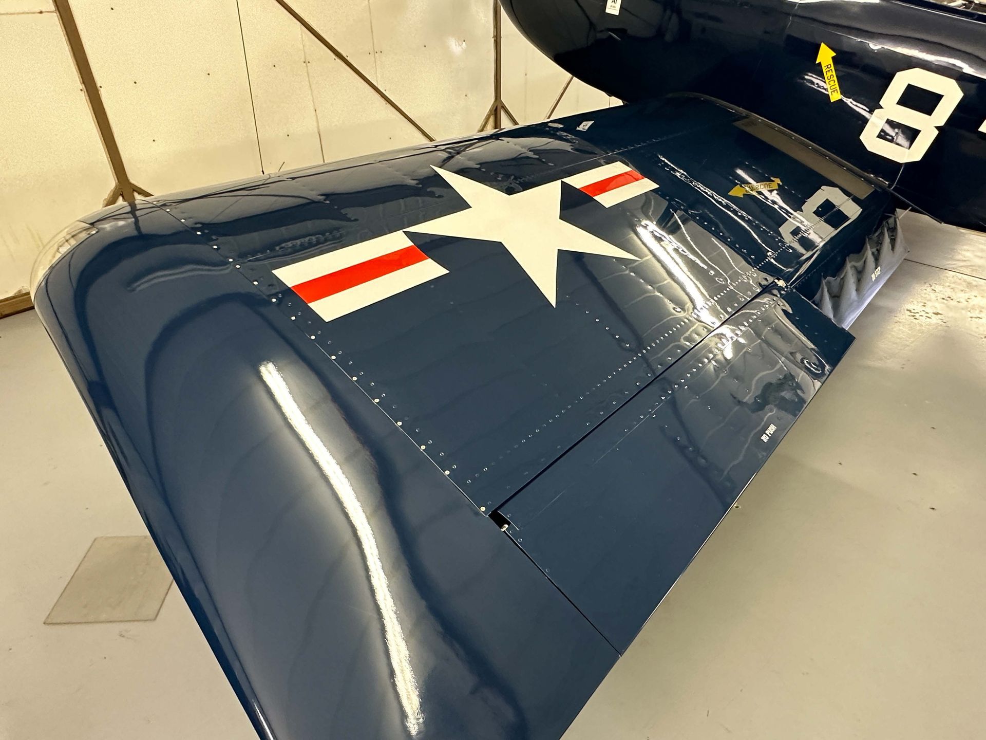 Blue airplane wing with white star, red stripes, and black markings, indoors.