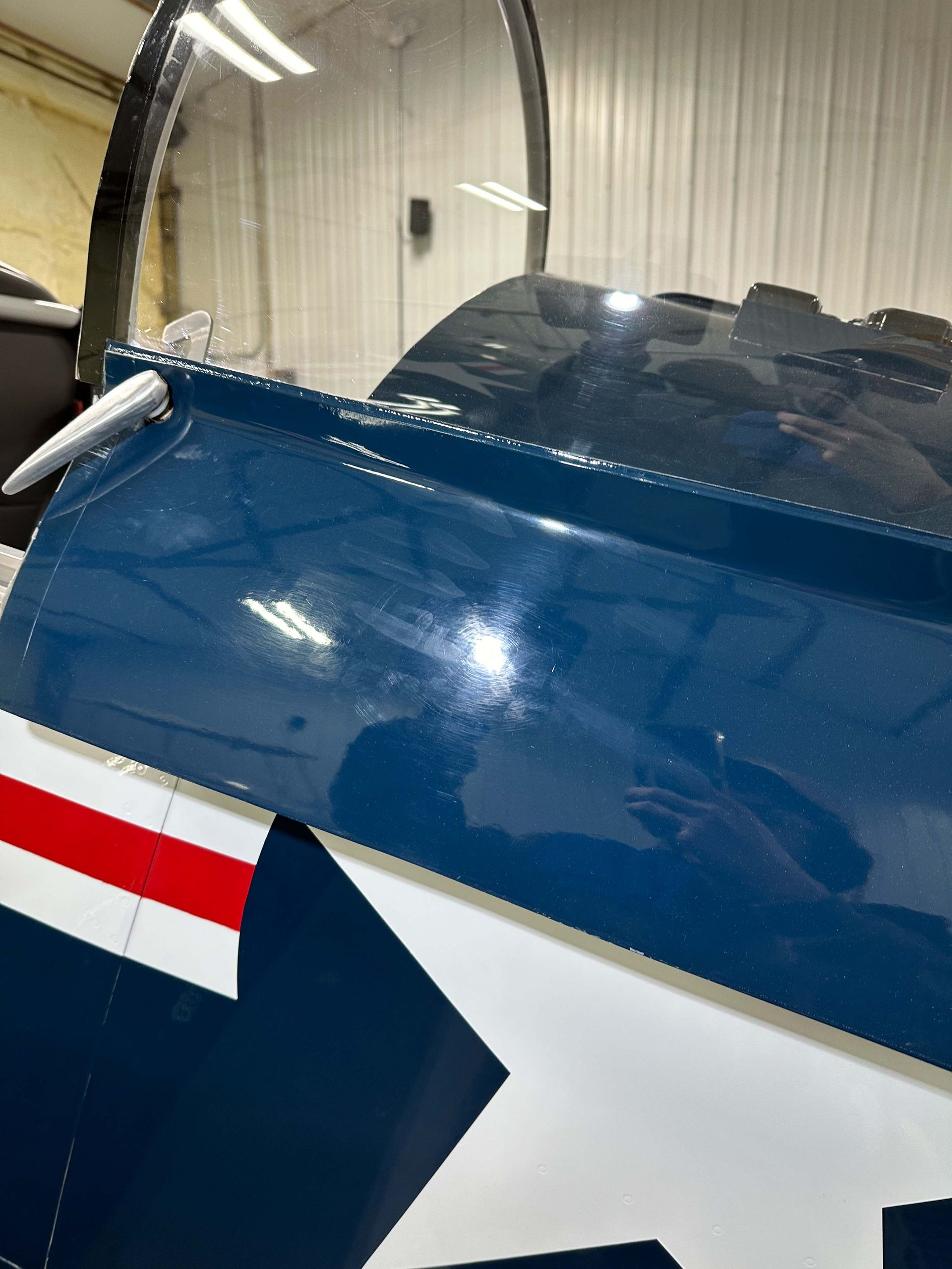 Blue and white airplane wing with red stripes and cockpit glass in a hangar.
