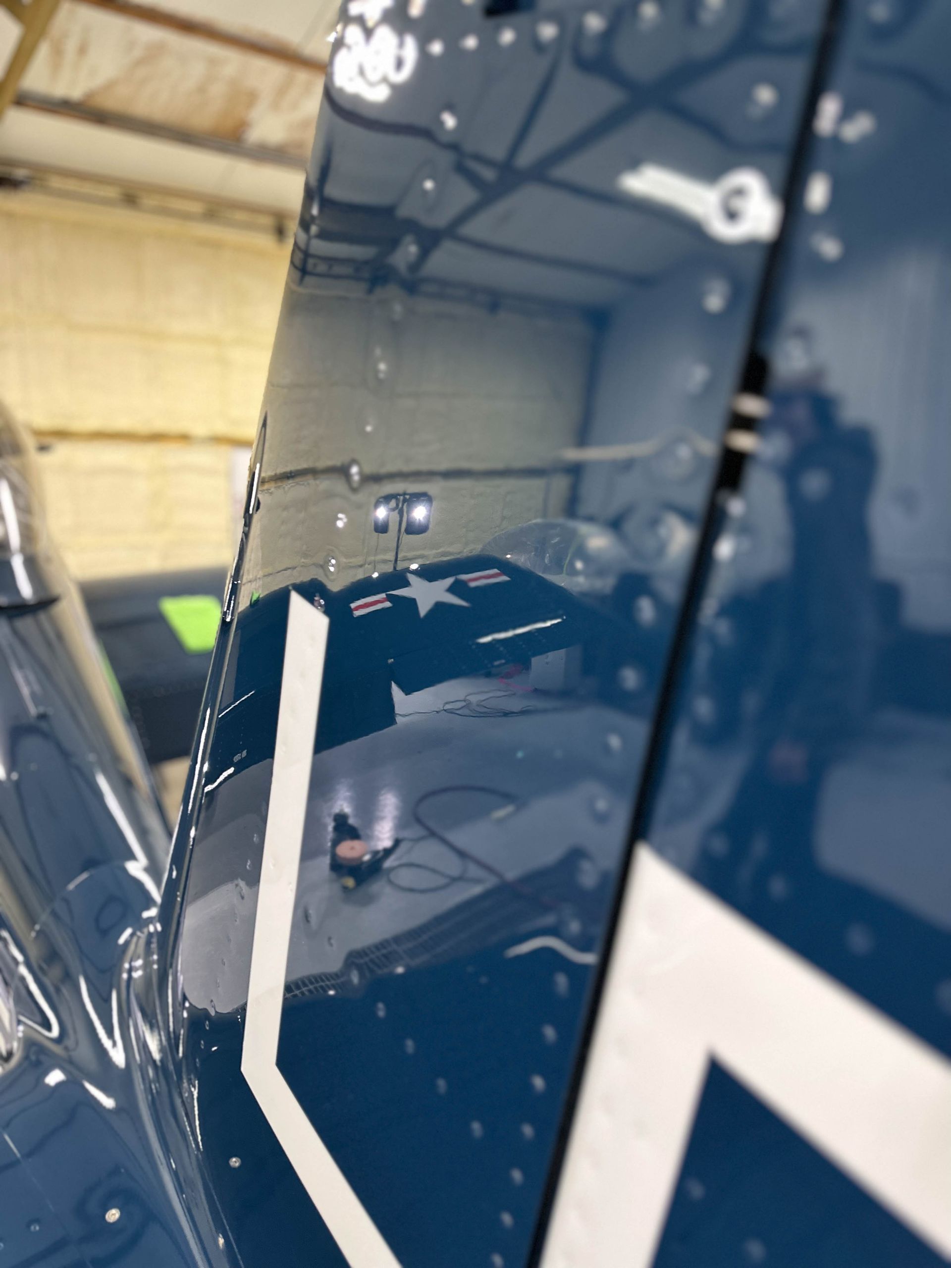 Blue airplane tail with white markings, rivets visible, indoors.