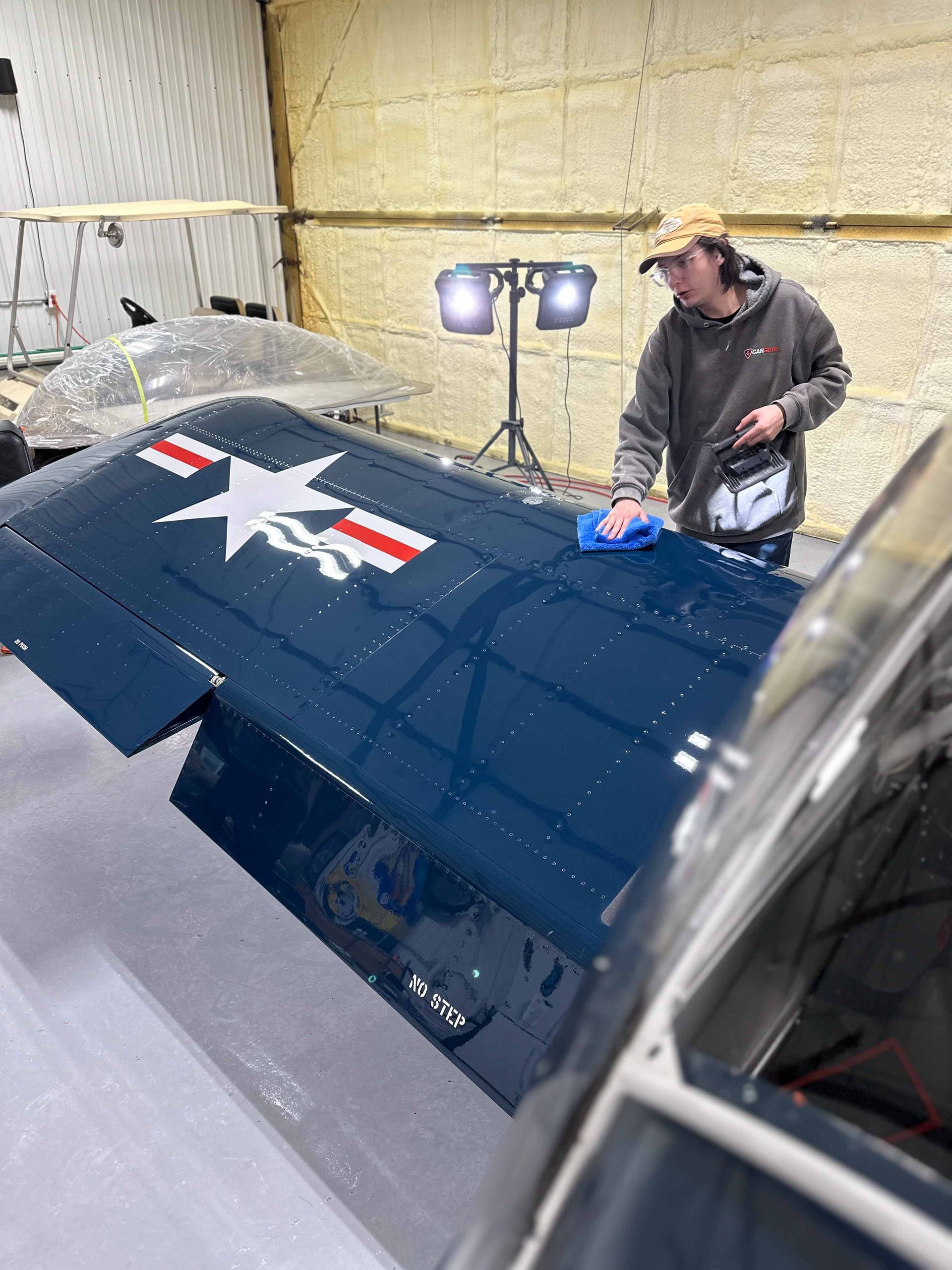 Man cleaning the wing of a blue airplane with a white star insignia in a hangar.