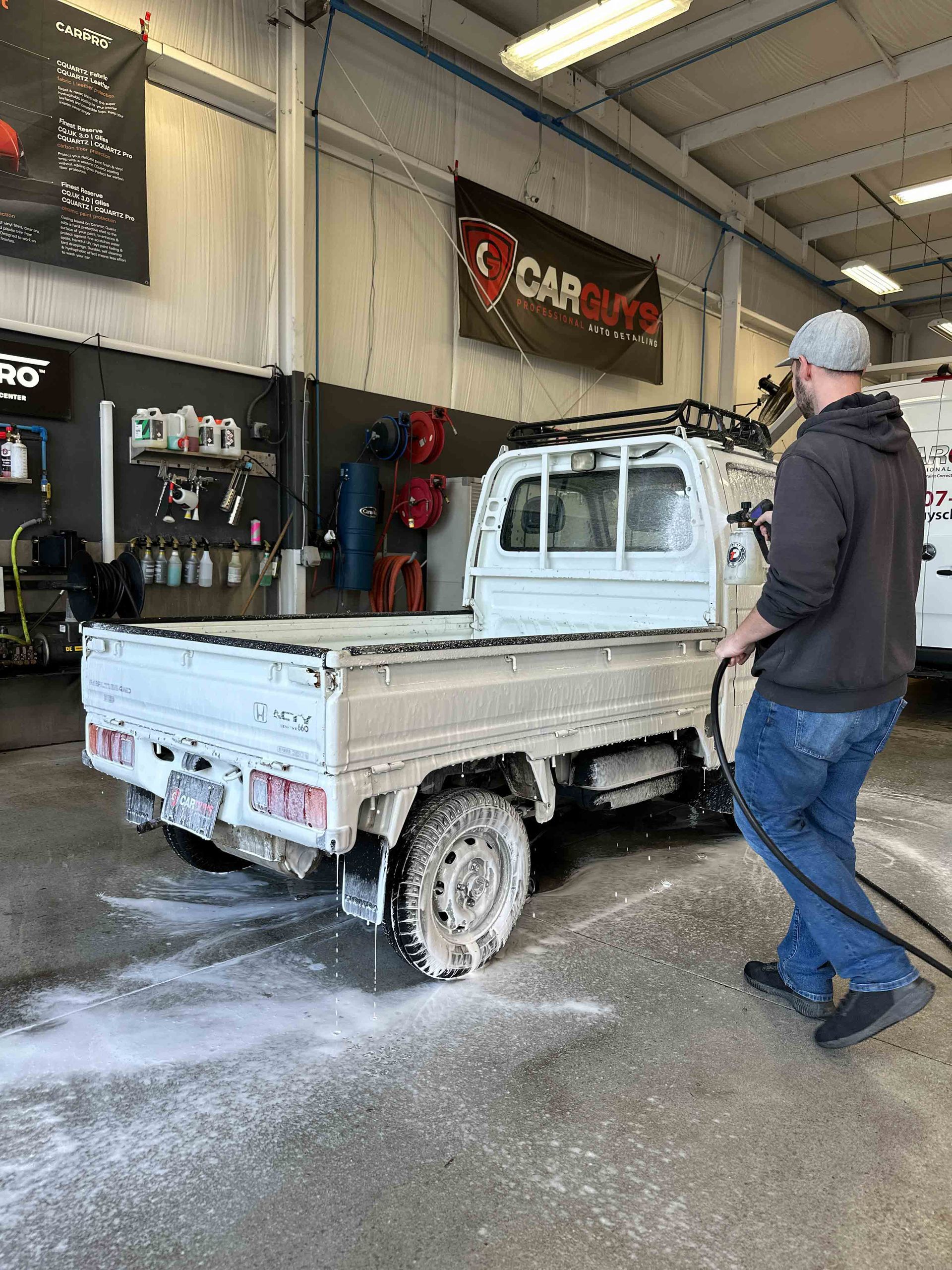 A person is using a blue squeegee to remove plastic from the hood of a car
