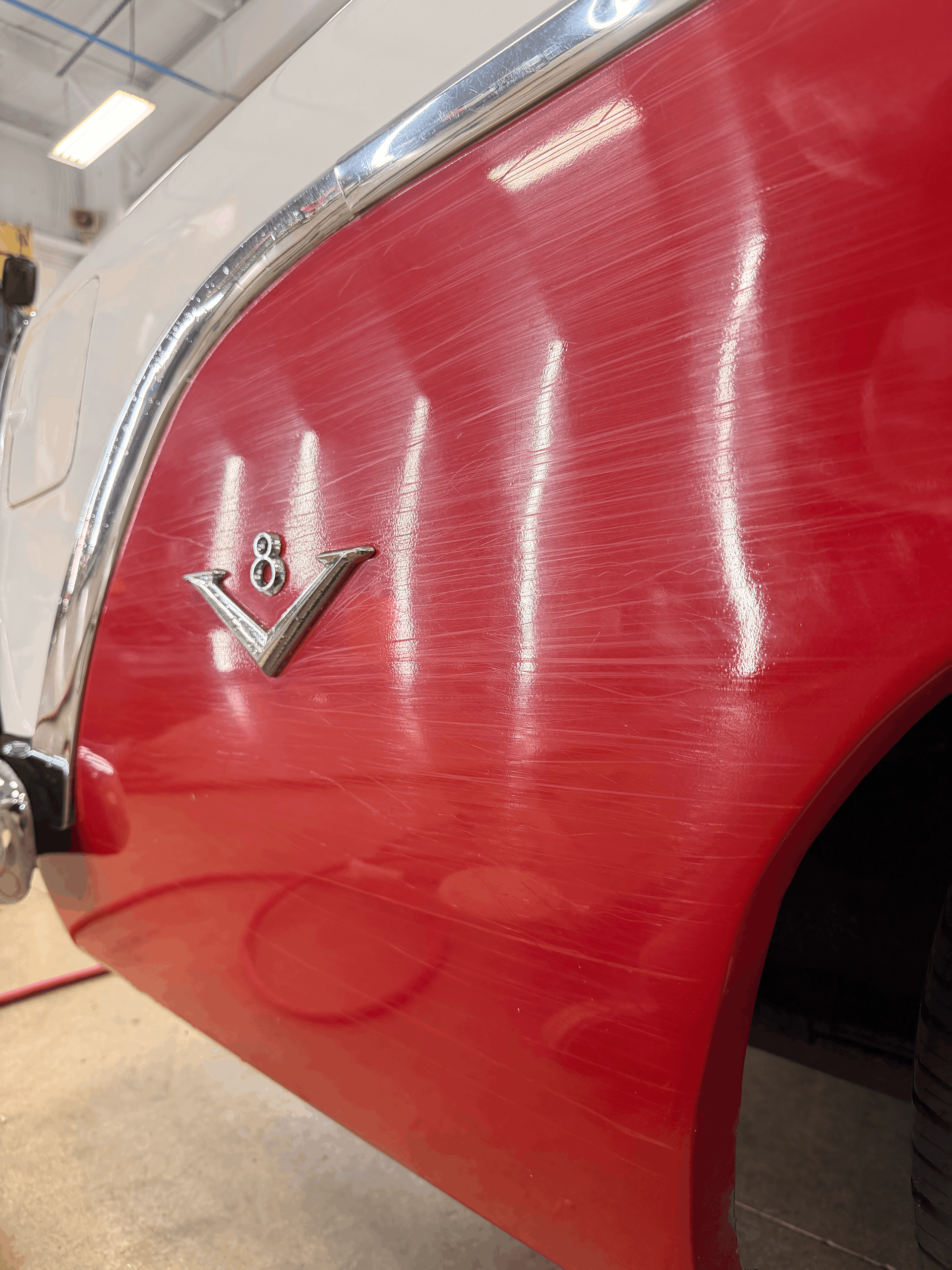 Red and white classic car's side panel with scratches, chrome trim, and emblem.