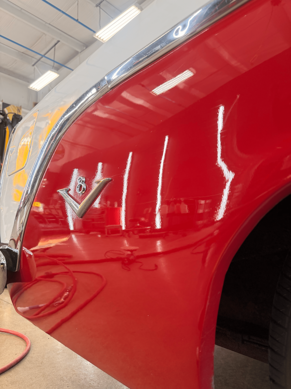 Red car fender with chrome trim, reflecting overhead lights.