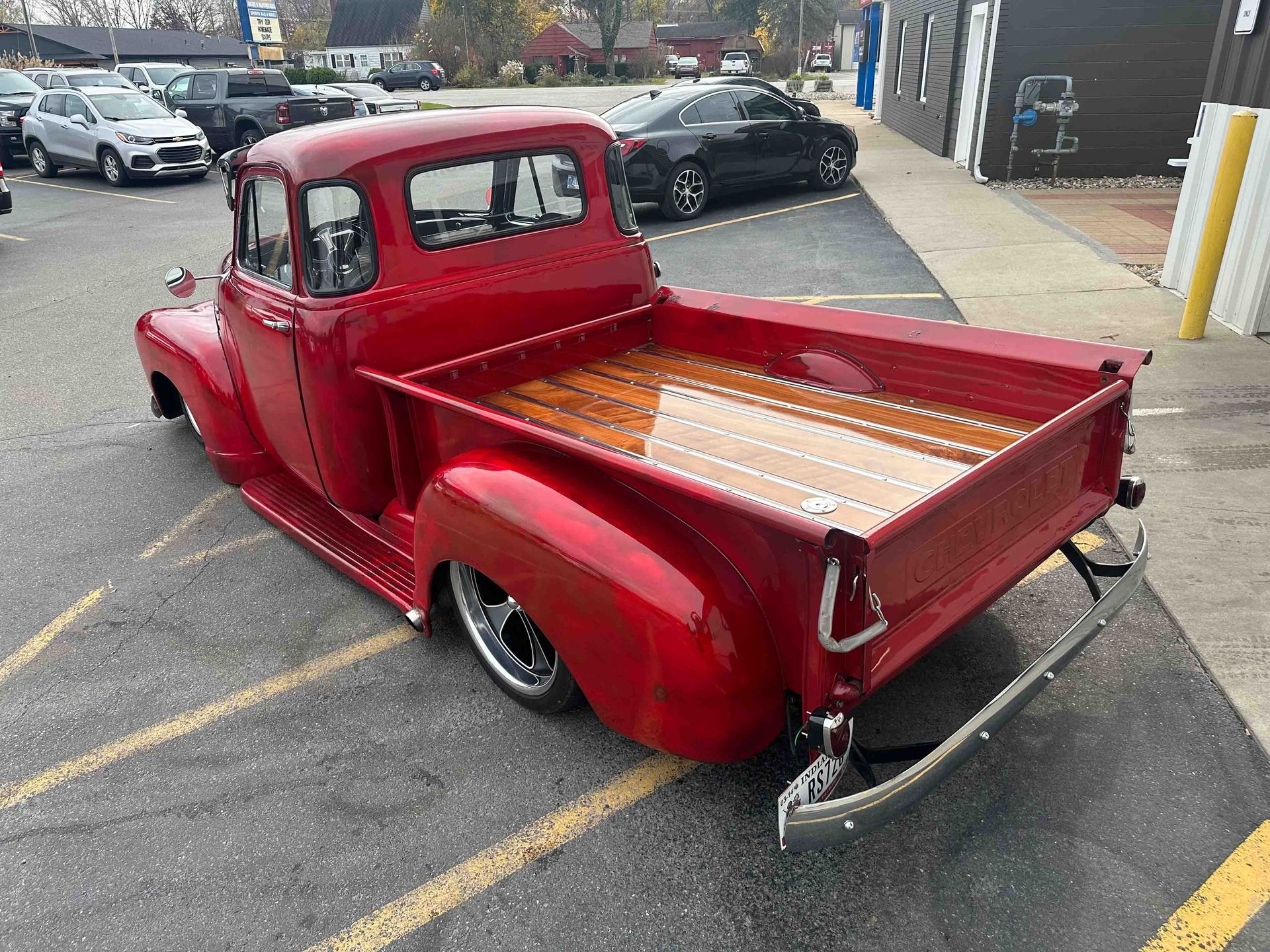 Red vintage pickup truck with a wooden bed parked in a parking lot.