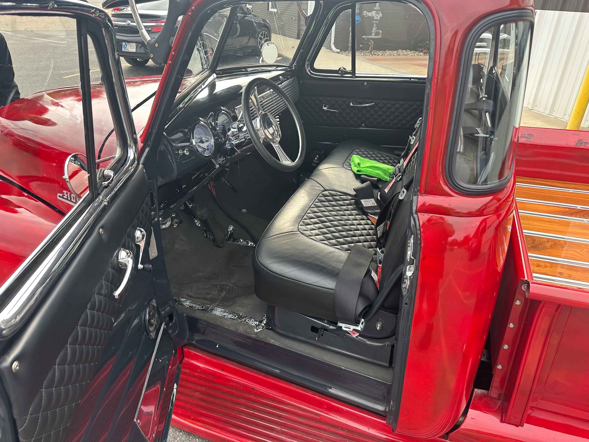 Red vintage truck interior with black quilted upholstery, chrome details, and open door.