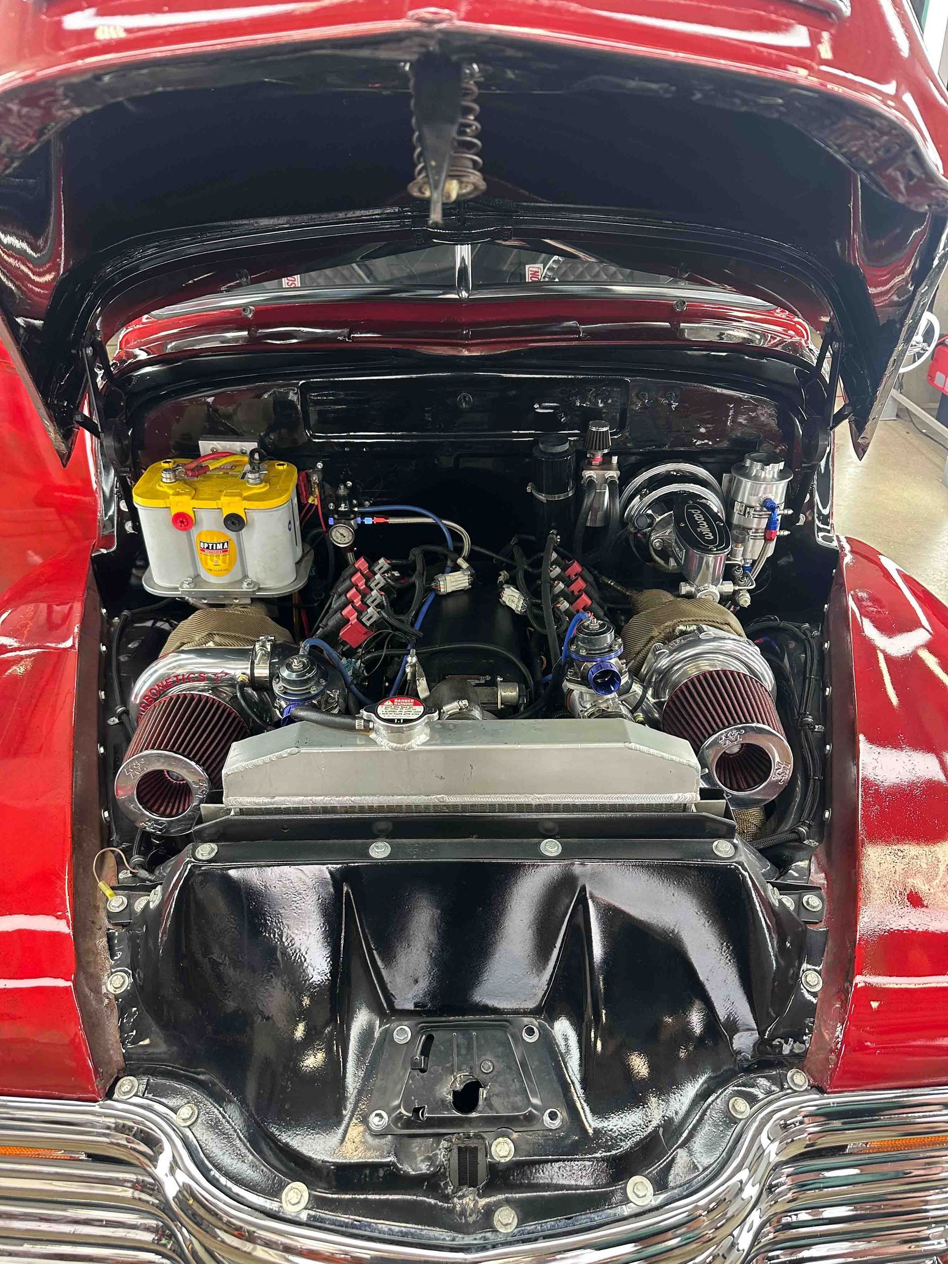Red car engine bay, black and chrome components, with twin turbochargers and a yellow battery.