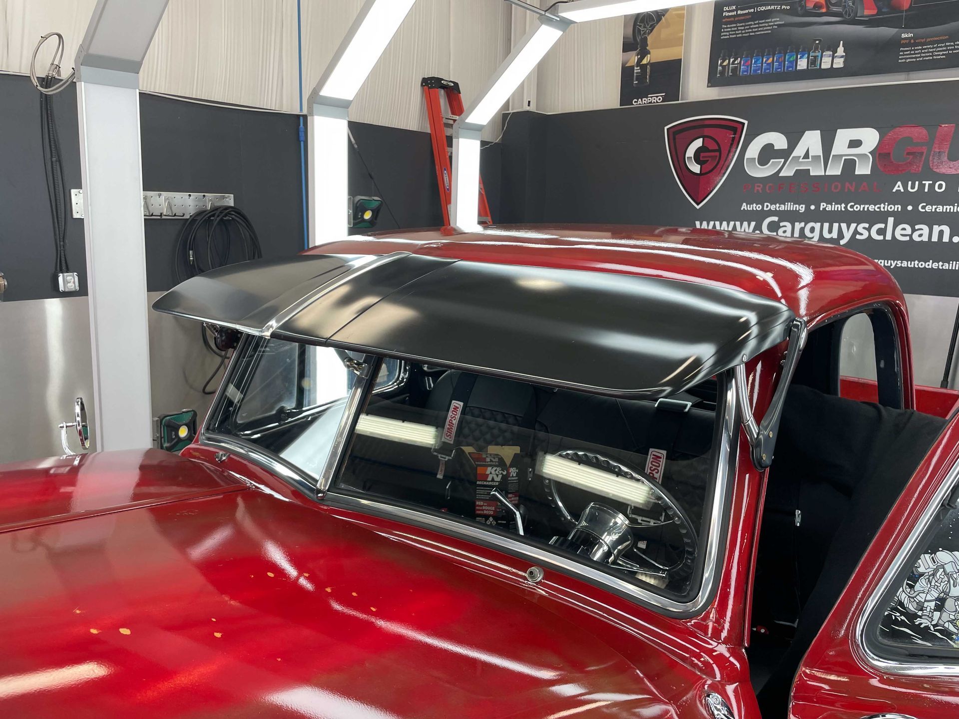 Red vintage truck with a black visor, inside a car detailing shop.