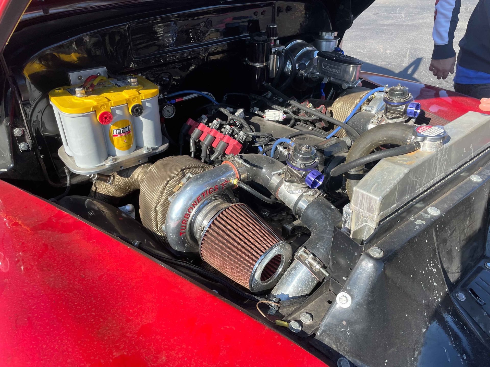 Red car engine bay with turbocharger and yellow battery.