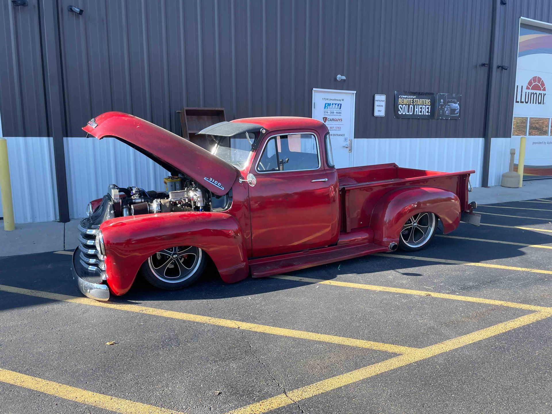 Red classic pickup truck with hood up, parked in a lot.