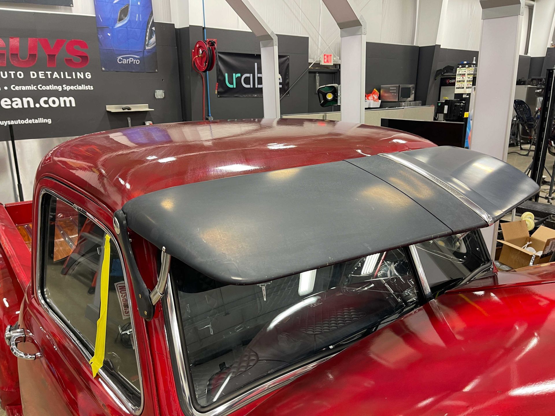 Red classic truck with a black sun visor installed in an auto detailing shop.