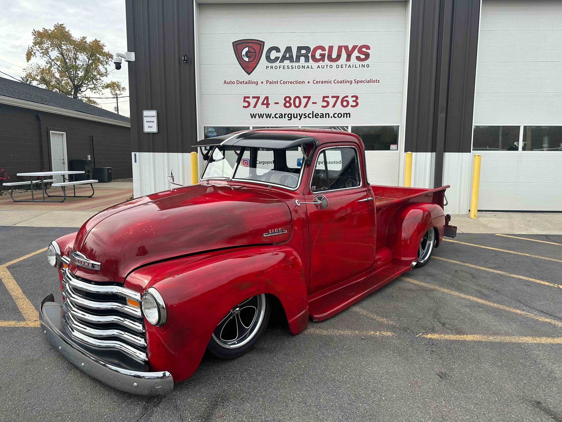 Red custom vintage Chevy pickup truck parked in front of Car Guys garage.