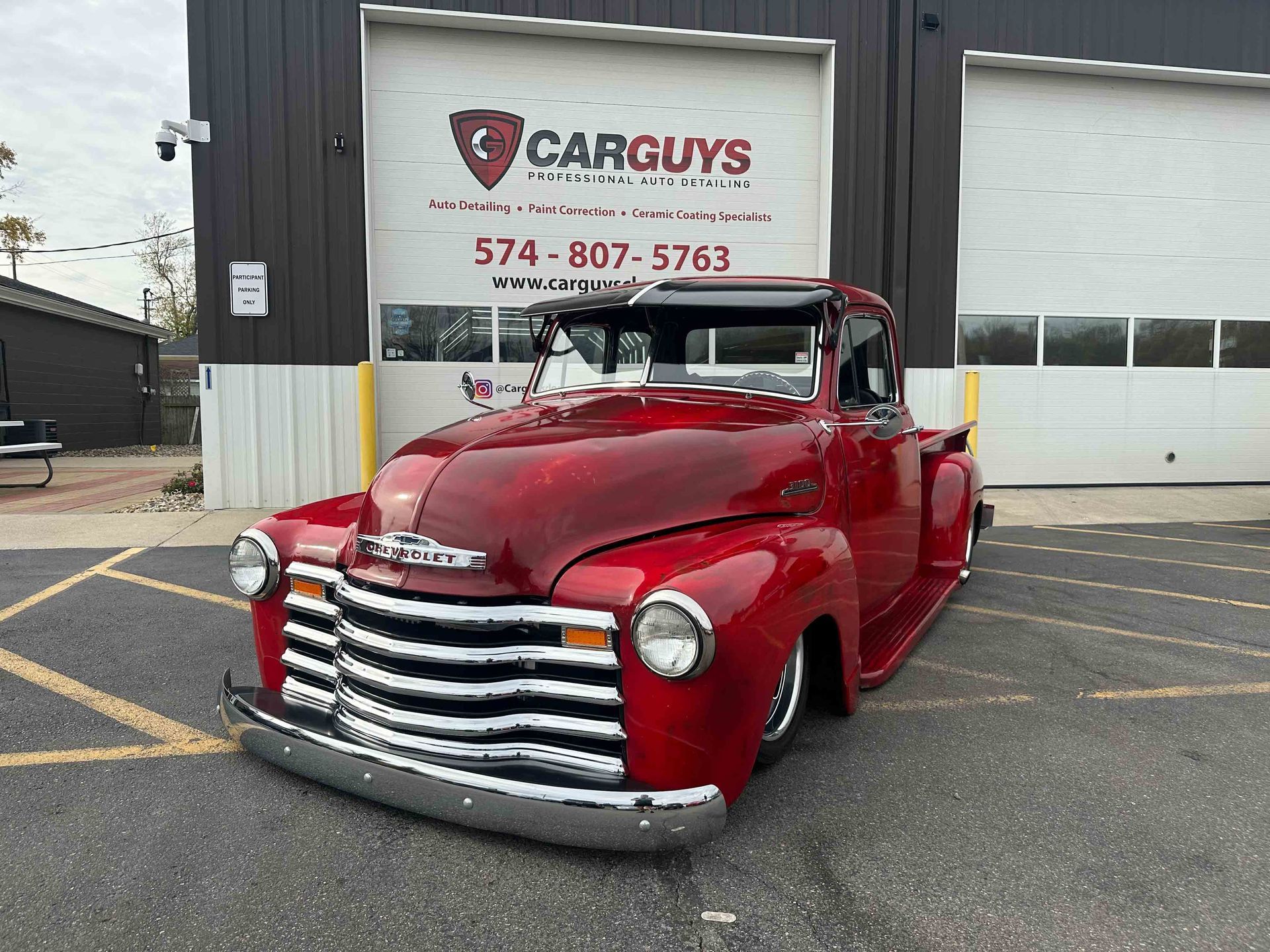 Red classic Chevrolet pickup truck parked in front of a car repair shop.