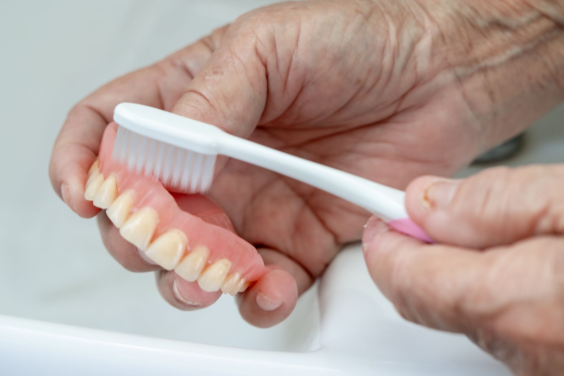 A person is brushing a denture with a toothbrush.