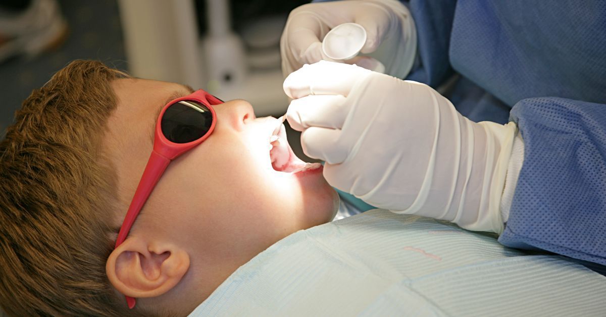 A young boy wearing red sunglasses is getting his teeth examined by a dentist.