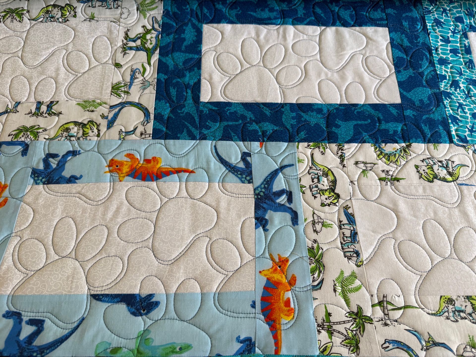 Quilted dinosaur fabric with paw print design in white and teal — Morning Star Quilting in Bateau Bay, NSW