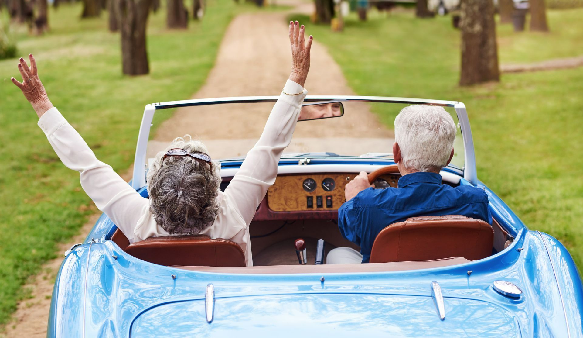 A man and a woman are sitting in a blue convertible car with their arms in the air. | The Villages, FL | My Transportation