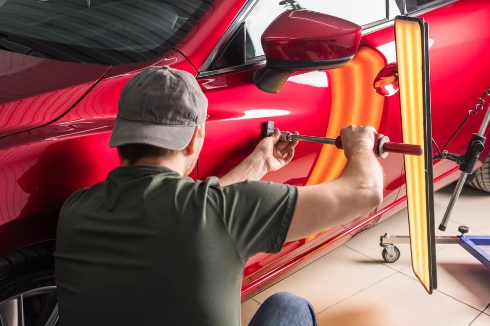 A Man Is Fixing a Dent in A Red Car — Chinderah Smash Repairs in Chinderah, NSW