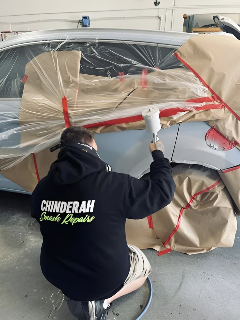 A Man Wearing a Hoodie Is Painting a Car — Chinderah Smash Repairs in Chinderah, NSW