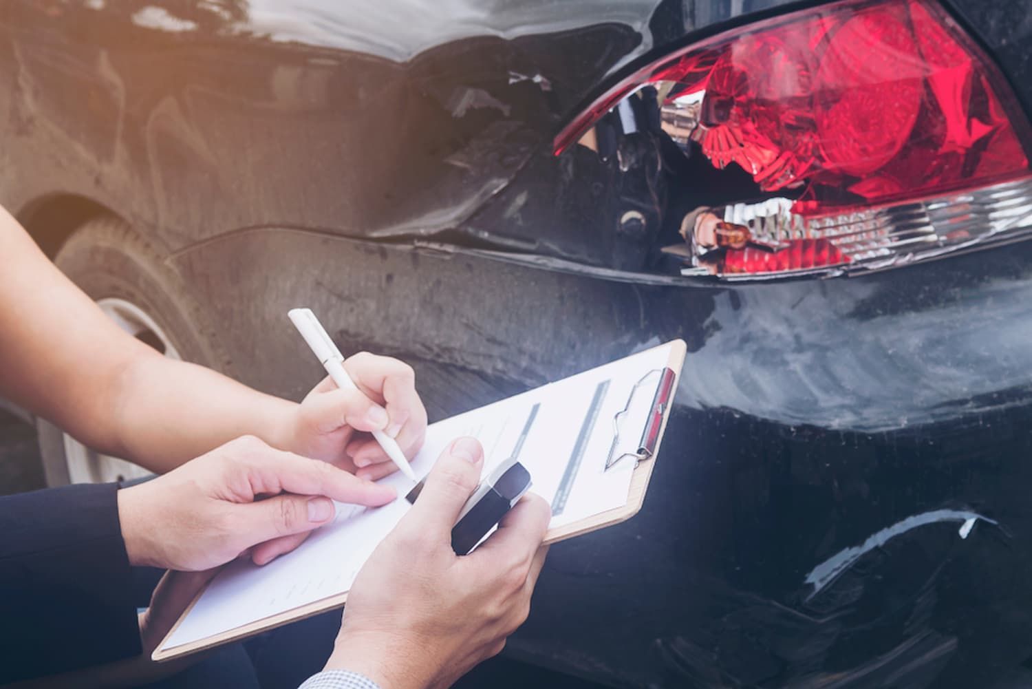 A Person Is Writing on A Clipboard in Front of A Car — Chinderah Smash Repairs in Chinderah, NSW
