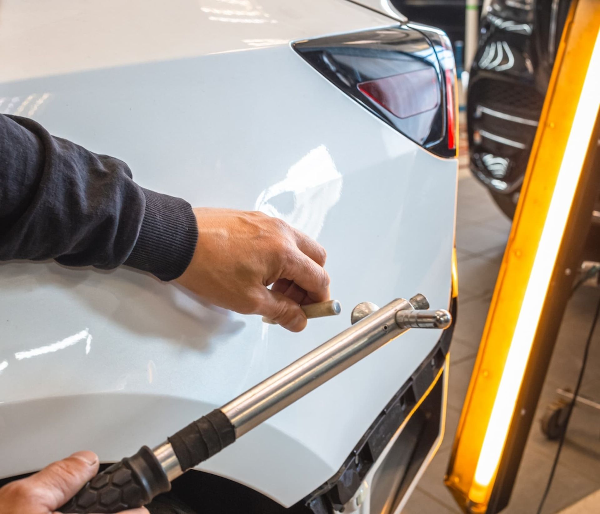 A Man Is Working on A White Car with A Tool — Chinderah Smash Repairs in Chinderah, NSW