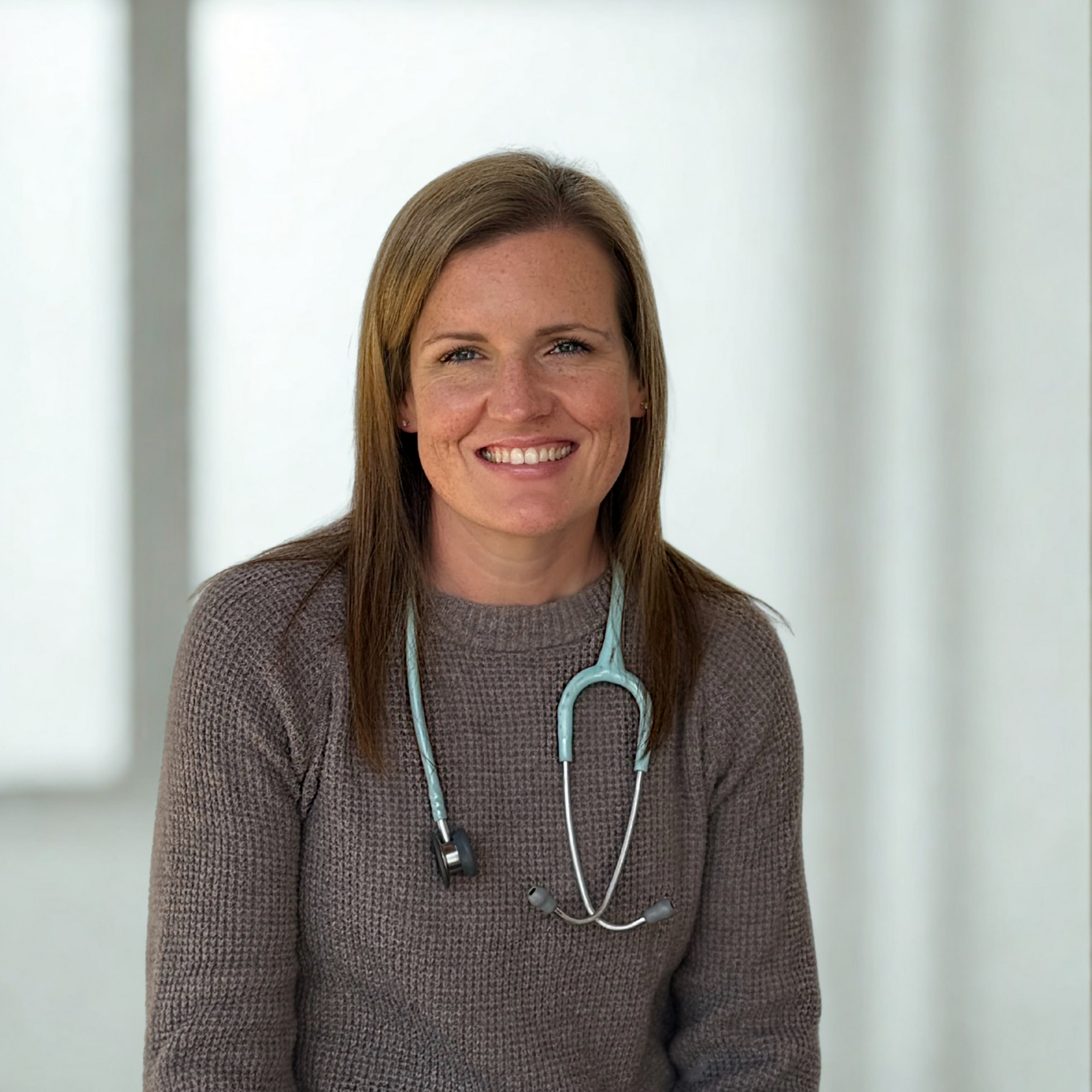 Woman doctor with stethoscope smiles in front of a blurred background.