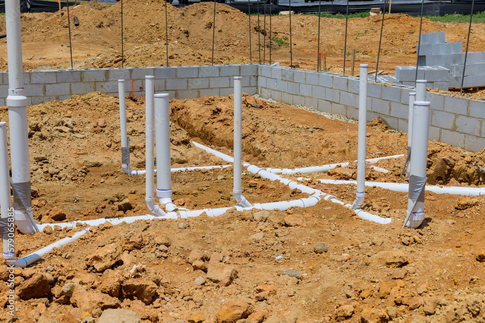 Foundation construction site with white PVC pipes, buried in brown dirt, and concrete block walls.