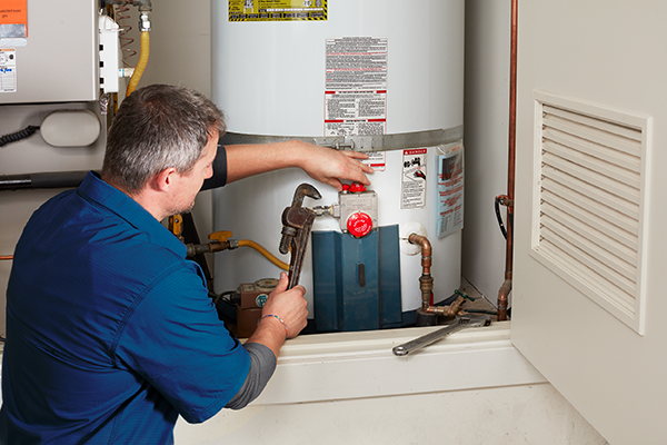 Plumber working on a hot water heater with a wrench in a utility room.