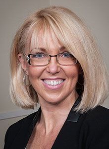 A woman wearing glasses and a black jacket is smiling for the camera.