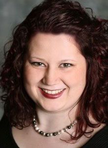 A woman with red hair and a pearl necklace is smiling for the camera.