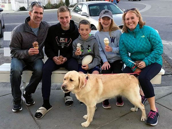 A family sitting on a bench with a dog and ice cream cones