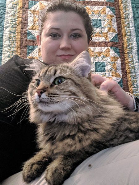 A woman is holding a cat in her lap in front of a quilt.