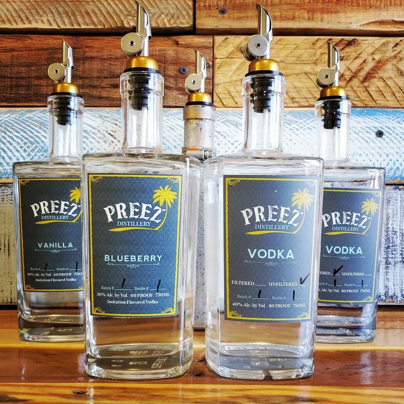 Five clear liquor bottles with black and blue labels and metal pour spouts