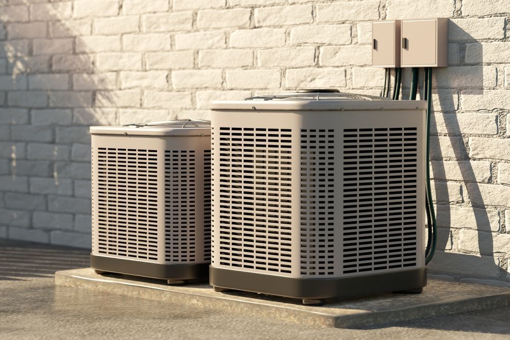 Two beige air conditioning units outside against a white brick wall, wires visible.