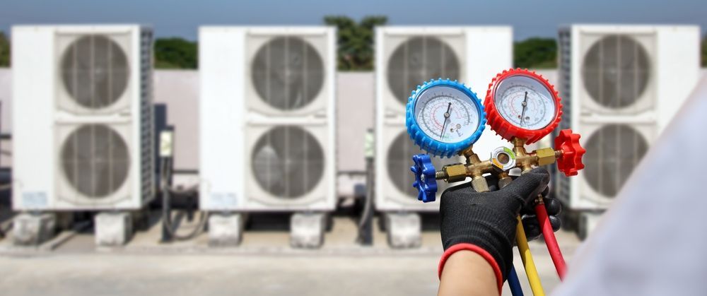 A technician uses gauges to service HVAC units on a roof.