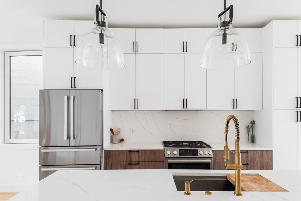 Modern kitchen with white upper cabinets, stainless steel fridge, and gold faucet.
