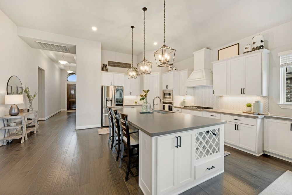 Modern white kitchen with island, pendant lights, dark wood floors, and stainless steel appliances.
